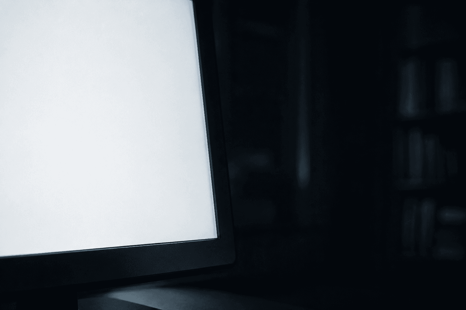 Close-up of a blank white computer monitor glowing in a dark room, screen empty